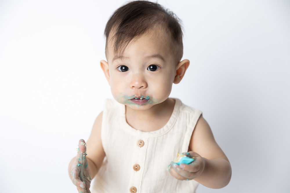 First Birthday Cake Smash photography - baby looking a bit innocent with a faceful of icing by Paper Bunny Studios Edmonton