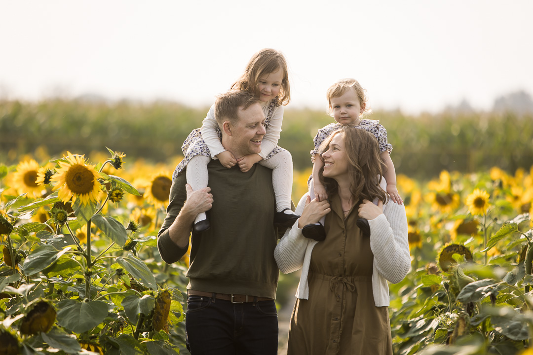 Edmonton family photos in sunflower field with daughters on mom & dads shoulders by fine art family photographer Paper Bunny Studios