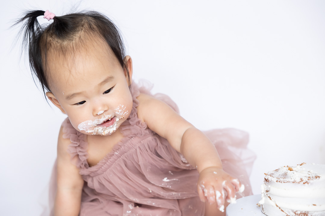 First birthday cake smash photography - baby reaching for cake with sticky fingers by Paper Bunny Studios Edmonton