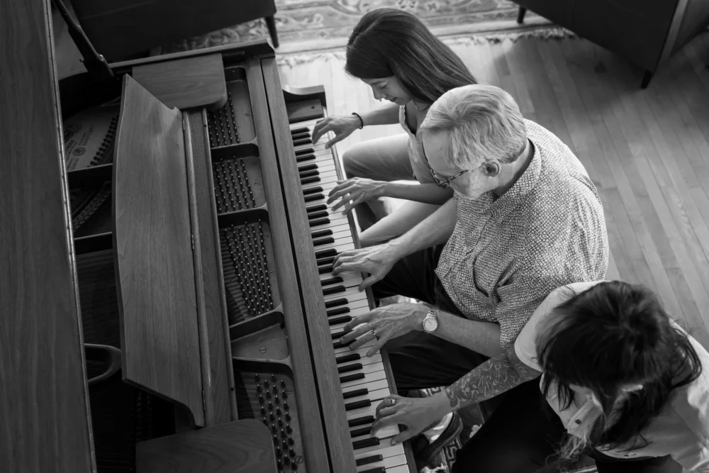 Black and white photo of stepdad and daughters playing the piano in the family home by documentary family photographer Paper Bunny Studios