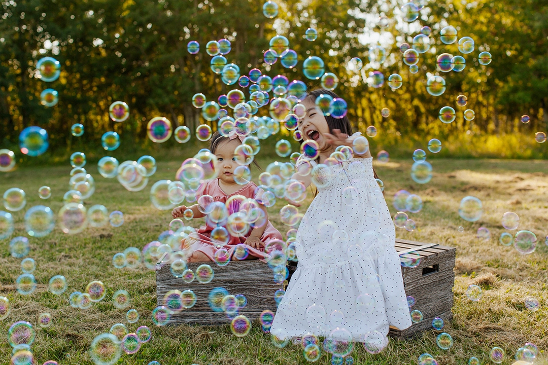 Outdoor family portrait of 2 girls and loads of bubbles in foreground by Edmonton Family Photographer Paper Bunny Studios