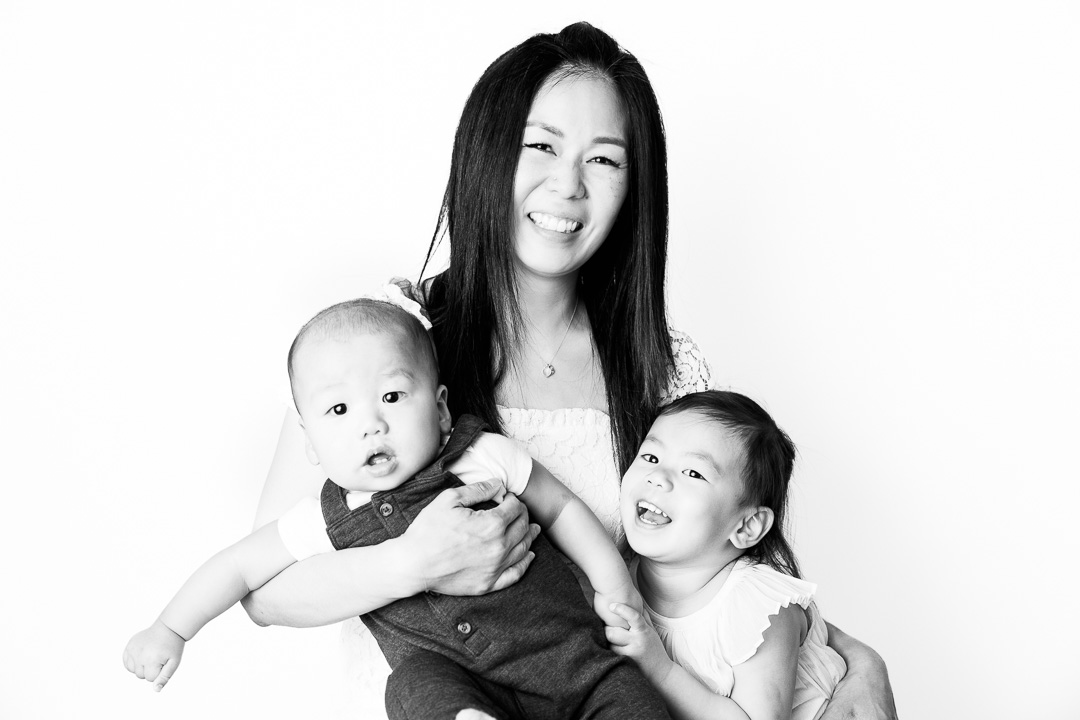 Black and white mother's day photo of mom with 2 kids against a white backdrop by Paper Bunny Studios Edmonton