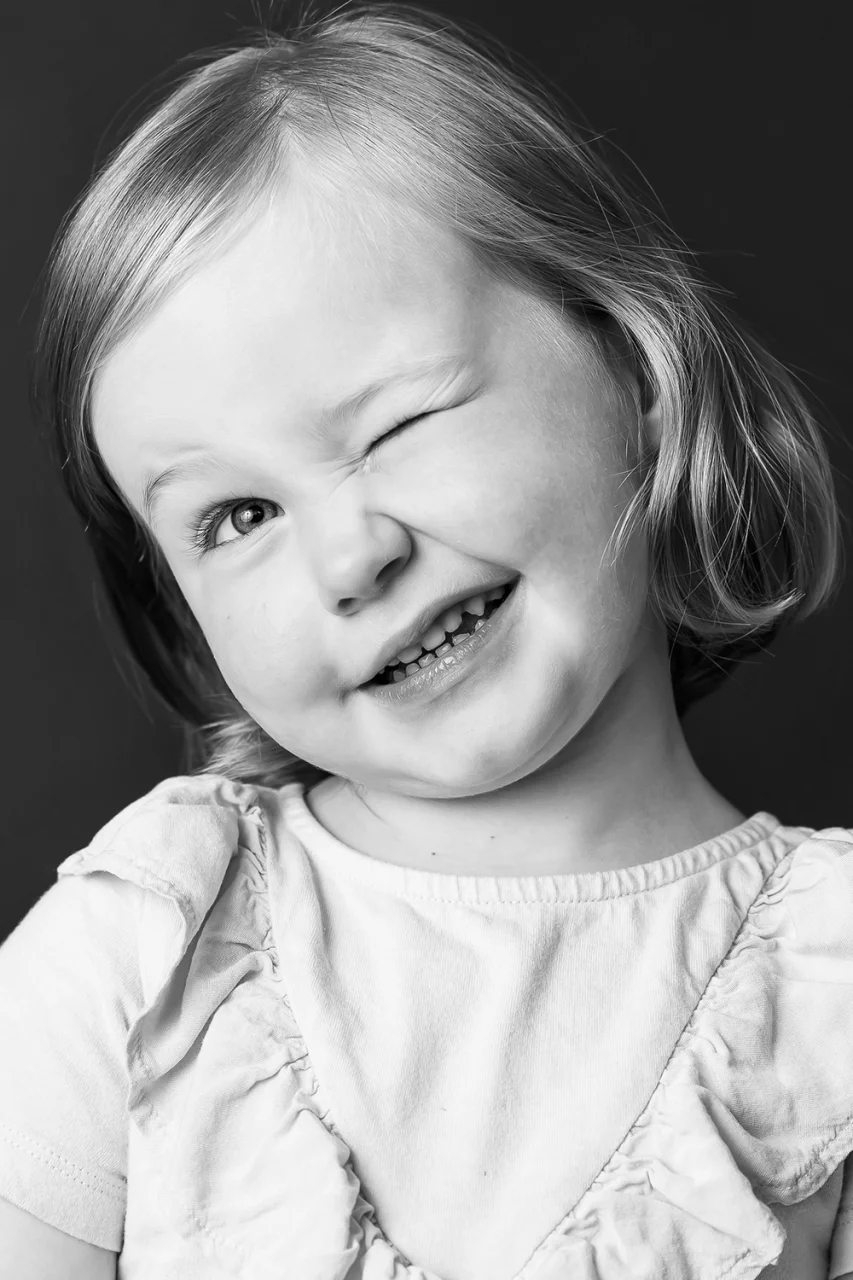 Black & white photo of little girl winking by Edmonton family photographer Paper Bunny Studios