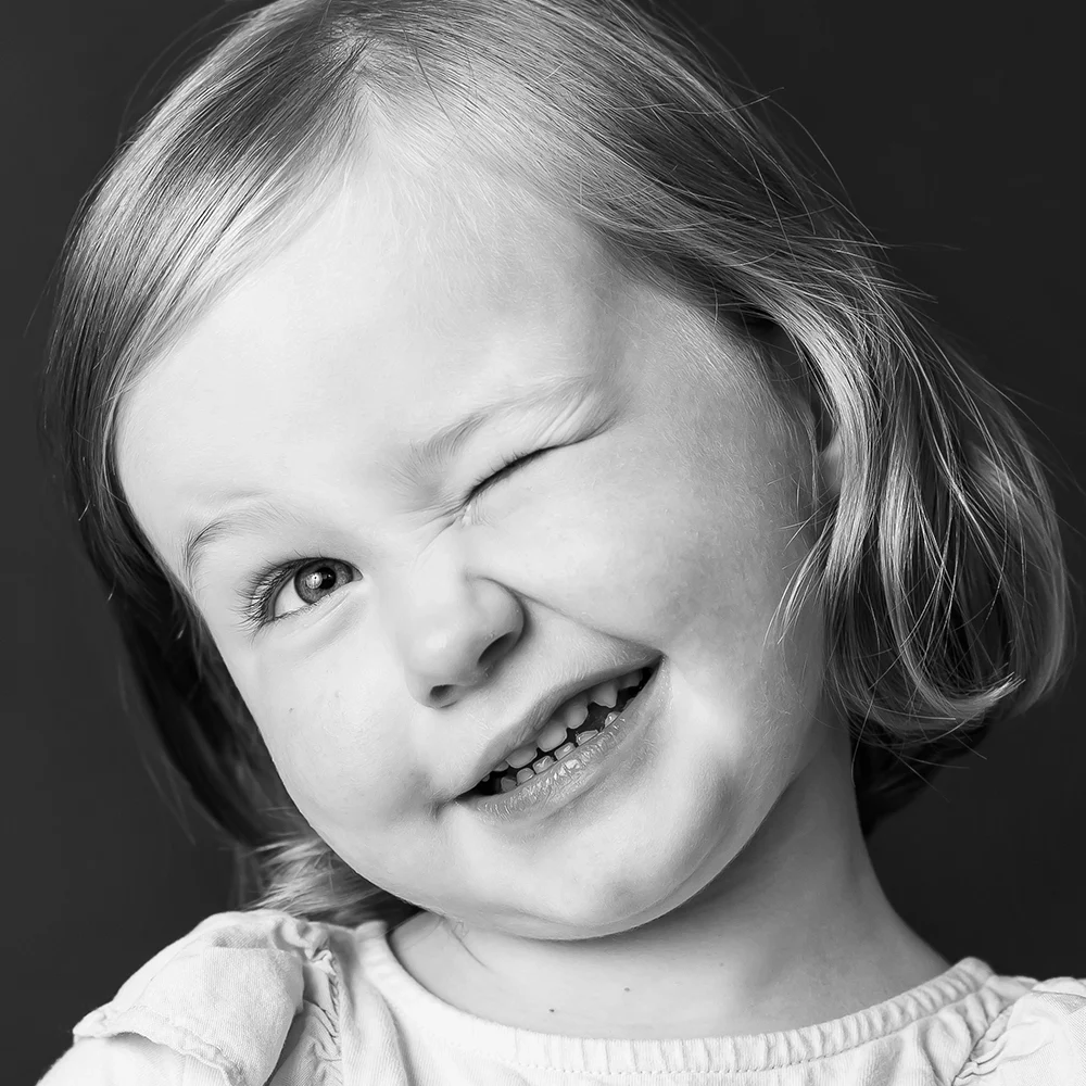 Black & white photo of little girl winking by Edmonton family photographer Paper Bunny Studios