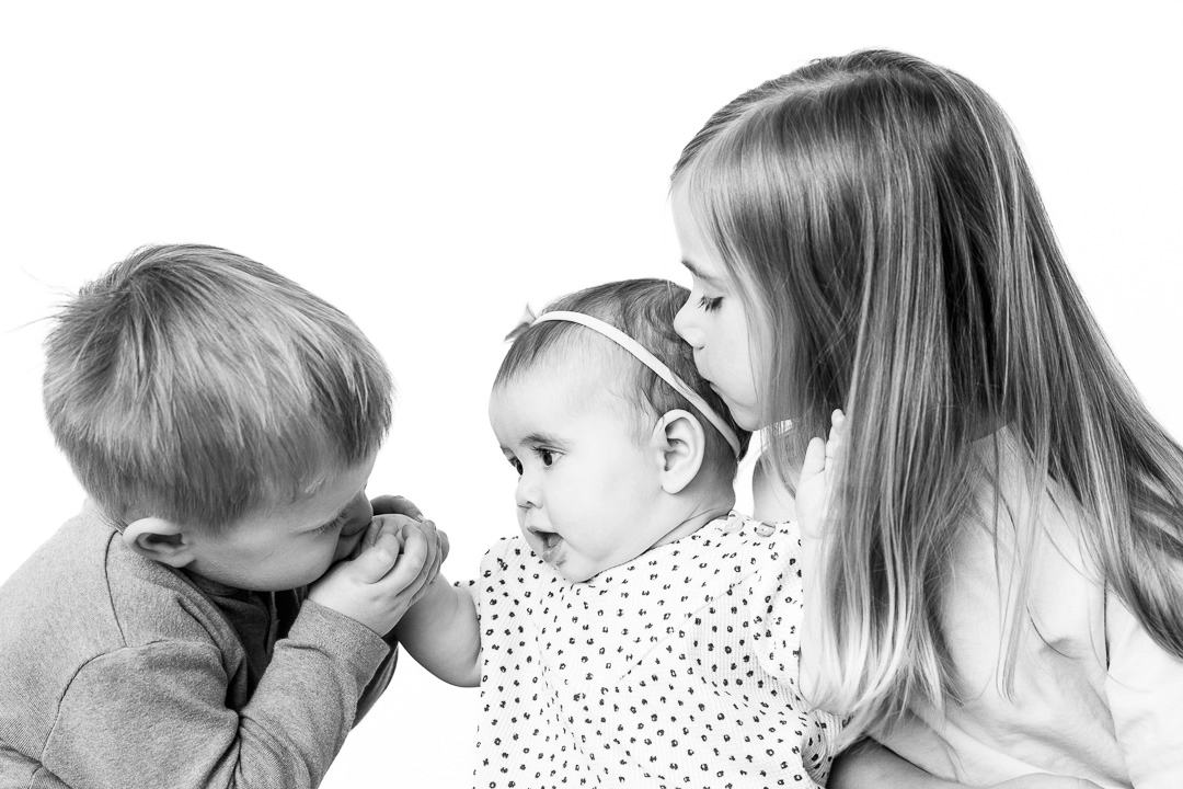 black and white kids portrait of 3 siblings showing older siblings being affectionate towards baby sister by Edmonton family portrait photographer Paper Bunny Studios
