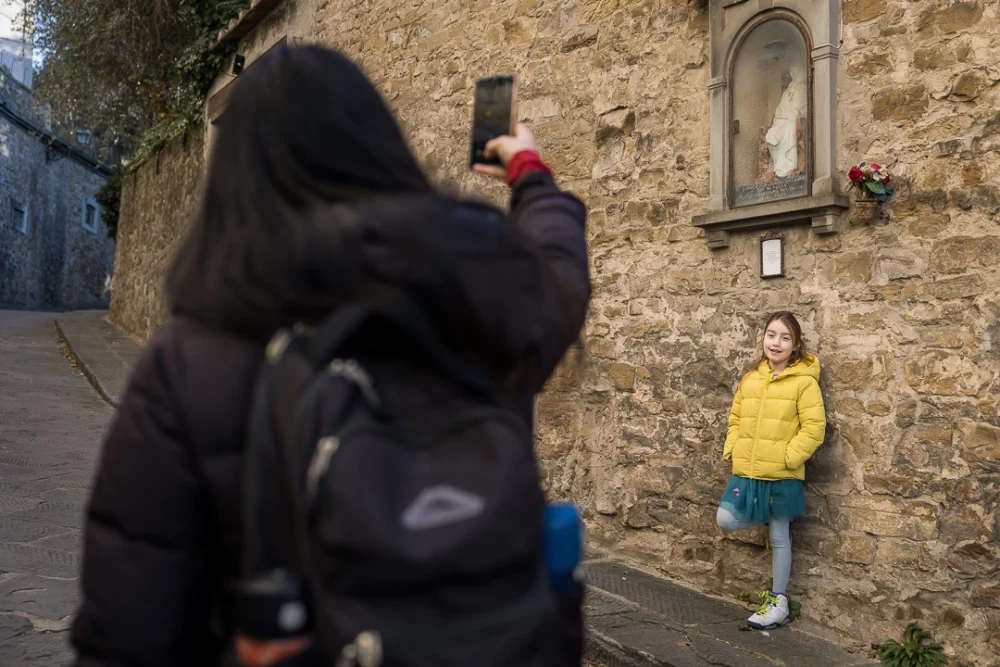 Documentary family photography of family on holiday - mom taking a photo of daughter leaning against a stone wall by Paper Bunny Studios Edmonton