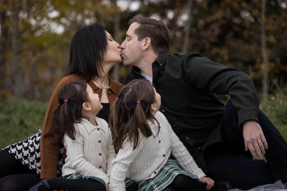 Mom & dad kissing with kids looking on by Edmonton Documentary family photographer Paper Bunny Studios