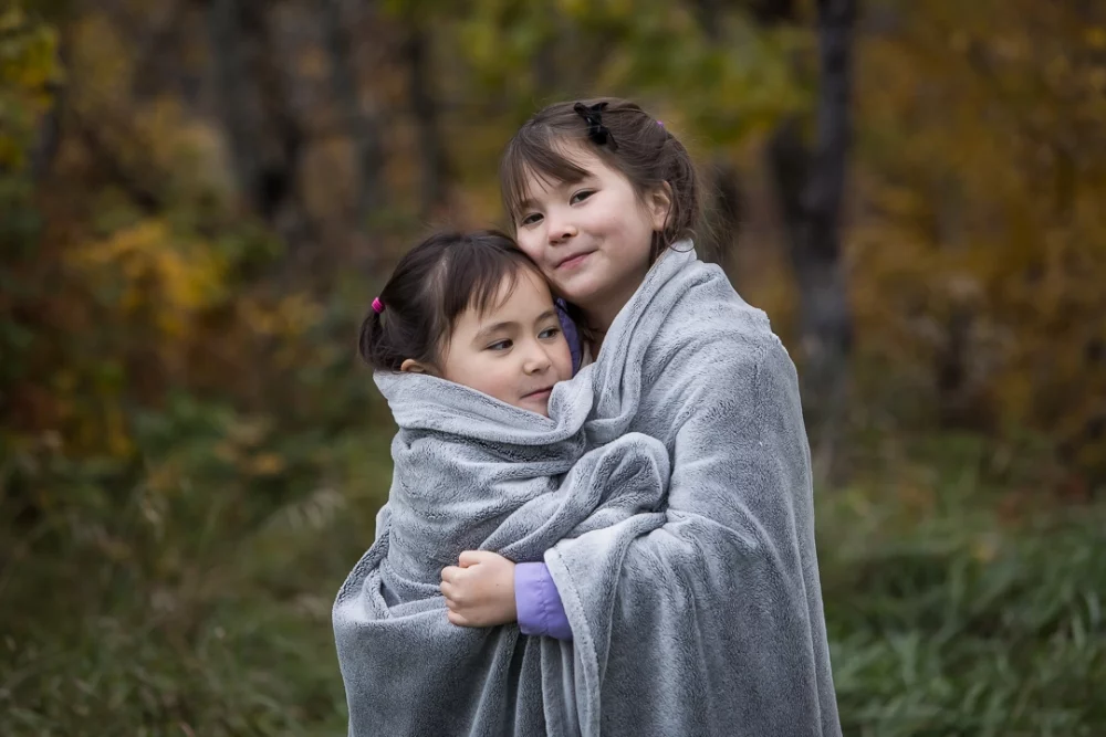 Sisters sharing a snuggly blanket during outdoor family photo shoot by Paper Bunny Studios Edmonton