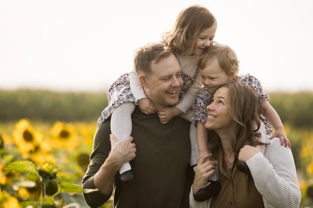 Edmonton family photos in sunflower field with daughters on mom & dads shoulders by fine art family photographer Paper Bunny Studios