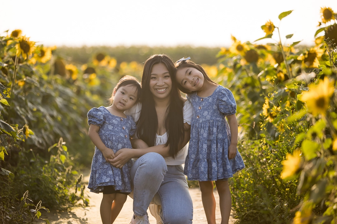 Edmonton family photos in sunflower field with  mom & daughters facing camera by fine art family photographer Paper Bunny Studios