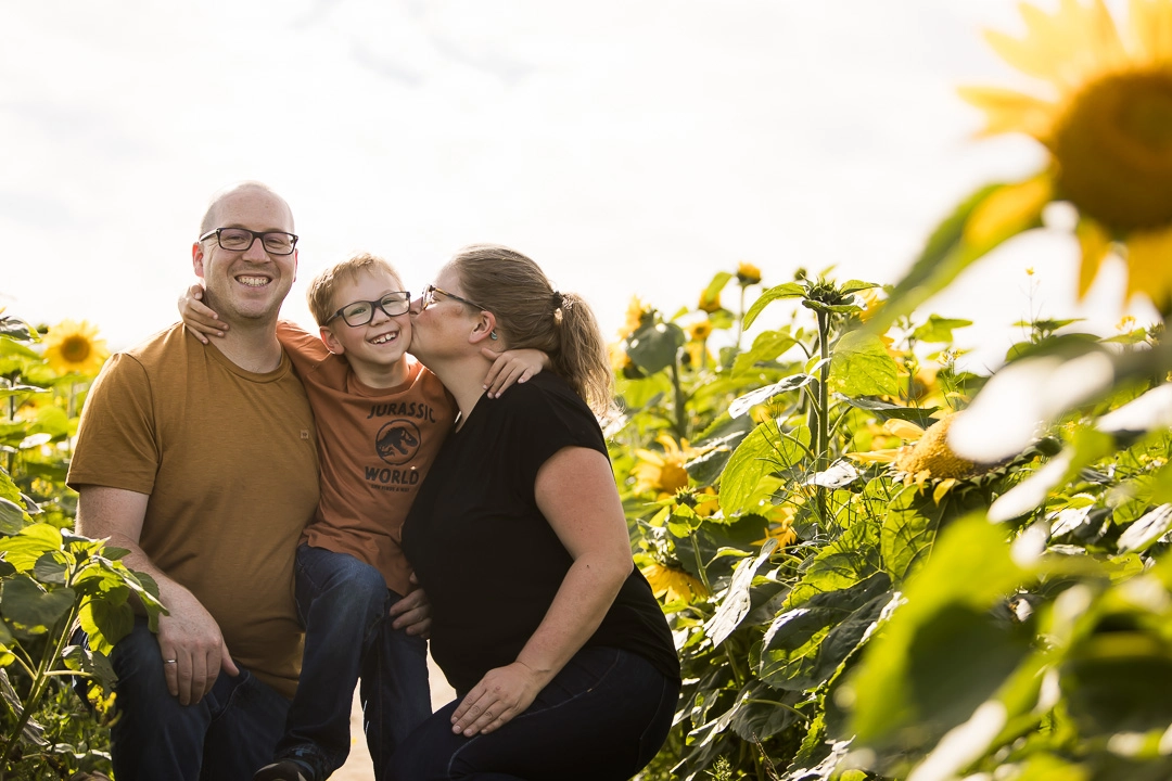 Edmonton family photos in sunflower field of mom kissing son on cheek by fine art family photographer Paper Bunny Studios