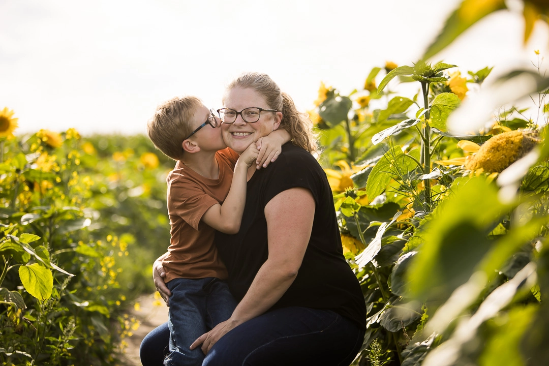 Edmonton family photos in sunflower field of son kissing mom on cheek by fine art family photographer Paper Bunny Studios