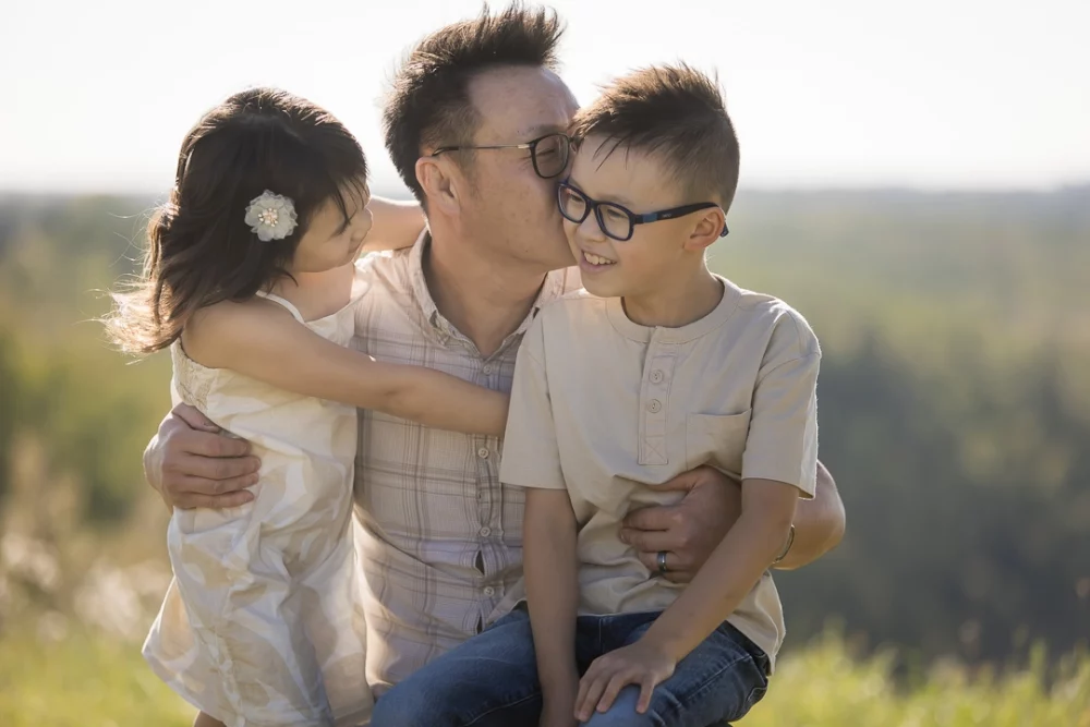 Outdoor family portrait of dad with kids kissing son on cheek by Paper Bunny Studios Edmonton