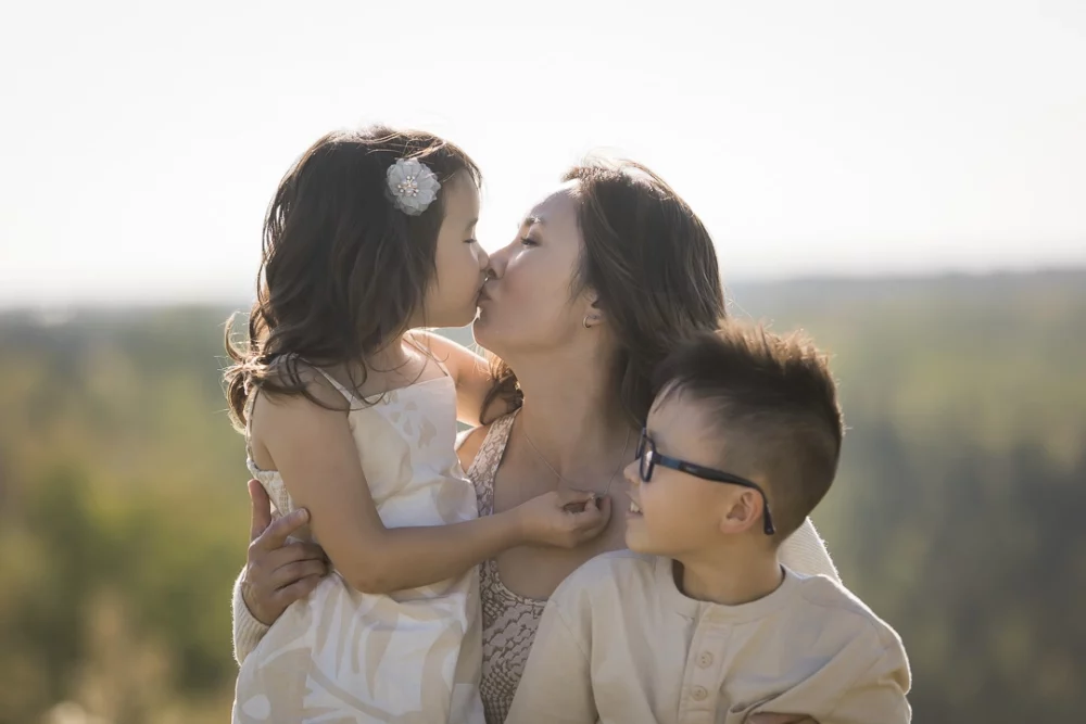 Outdoor family photo of mom kissing daughter by Paper Bunny Studios Edmonton