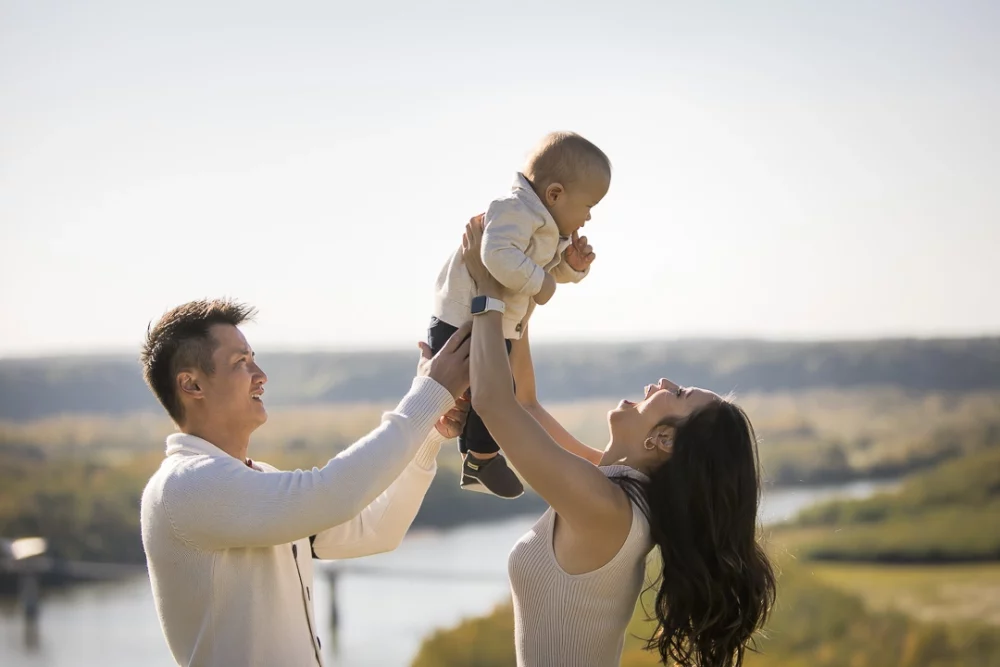 Outdoor family photo of parents with mom lifting baby up by Paper Bunny Studios Edmonton